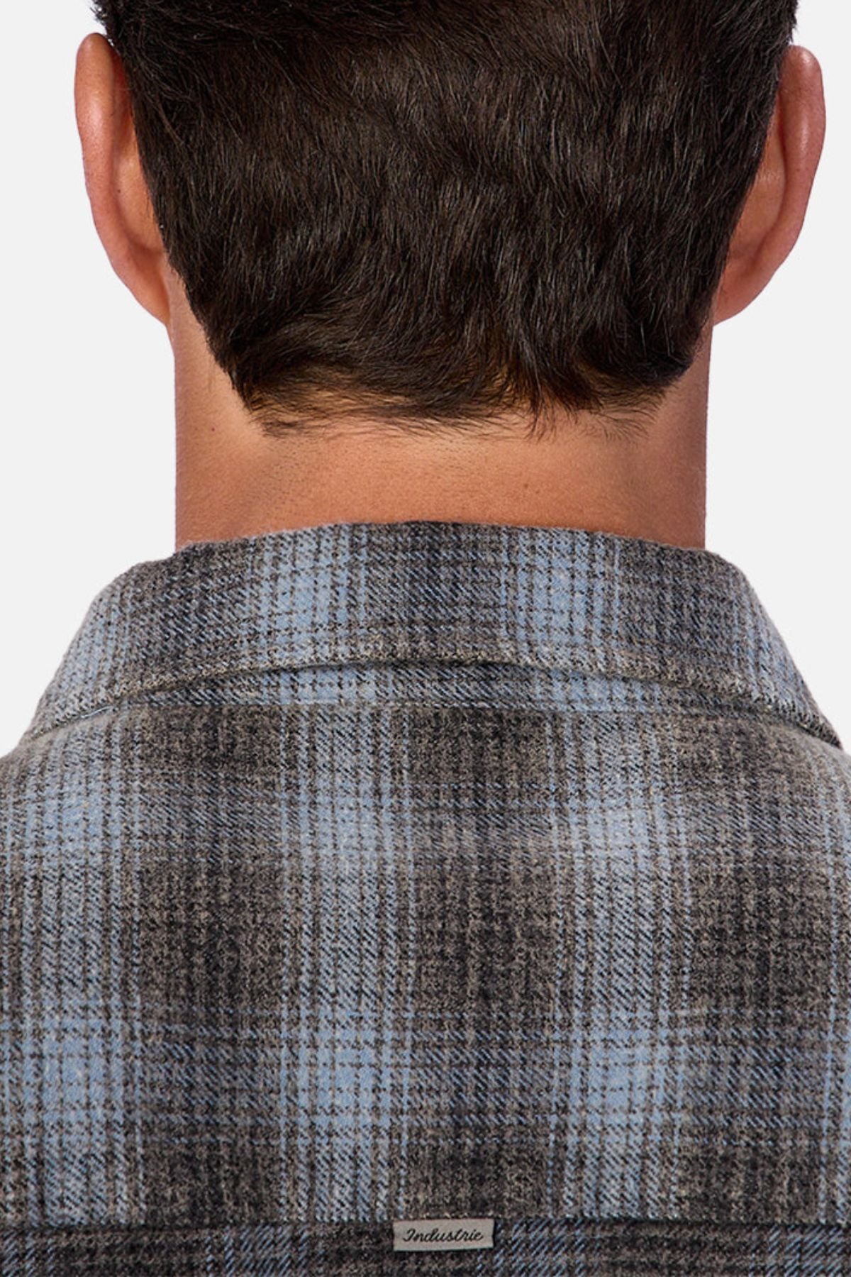 A close-up of the back of a person’s head shows short dark hair and the collar of the Industrie Durango Long Sleeve Shirt in blue and gray plaid cotton, featuring a small label—a wardrobe essential.