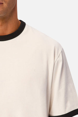 Close-up of a person wearing the Industrie The Hudson Ringer Tee, featuring classic black trim around the crew neck. Only part of the person’s face, neck, and shoulder are visible against a plain background.