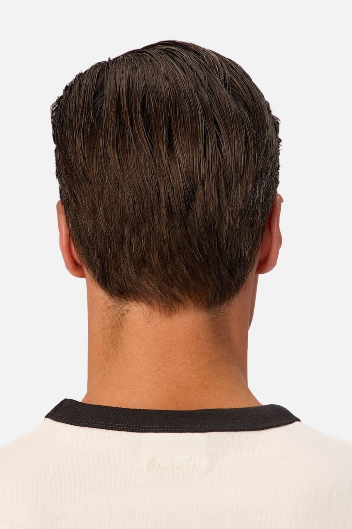 A man with short, dark brown hair is seen from behind, wearing the Industrie The Hudson Ringer Tee—a white shirt featuring a black collar and a classic crew neck. The background is plain and light-colored.