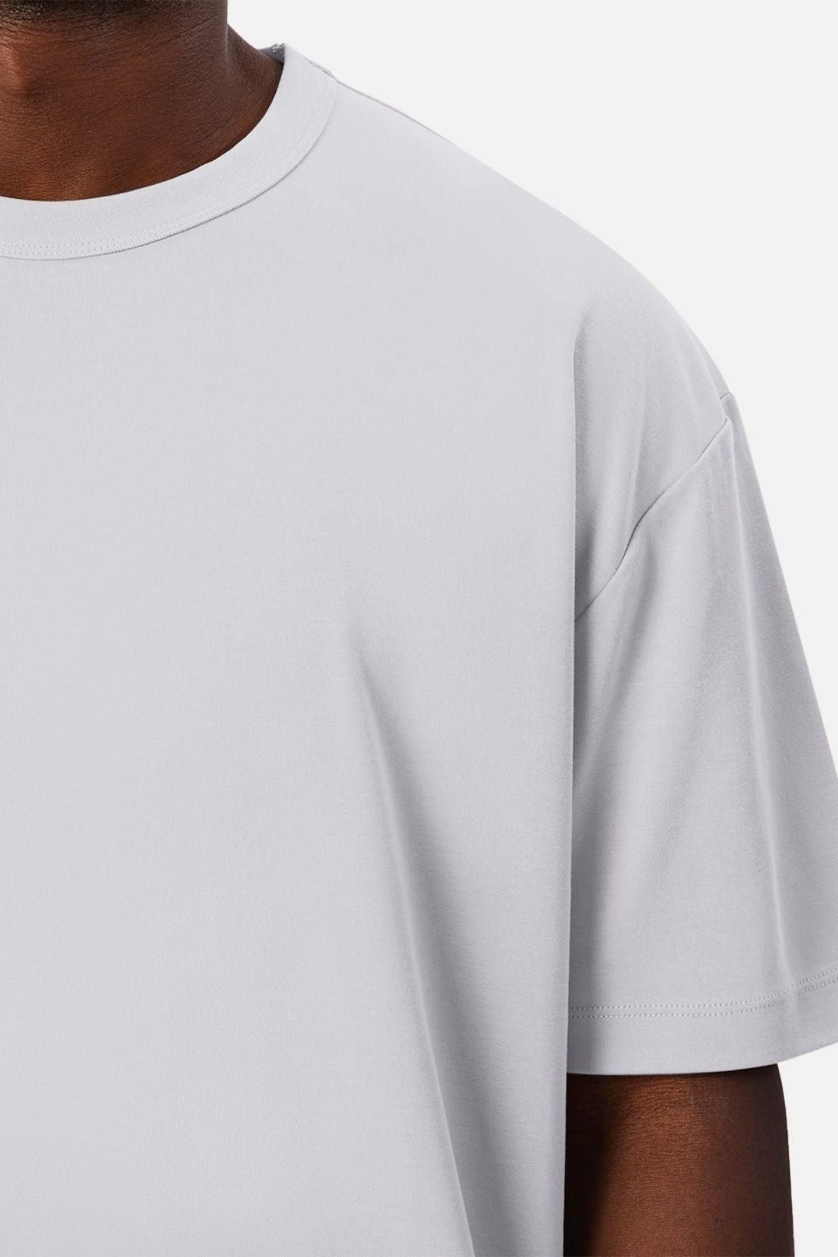 A close-up shows a person wearing the Industrie Luxe Del Sur Tee, highlighting the relaxed fit and 100% cotton fabric with a focus on the left chest, shoulder, and part of the neck against a white background.