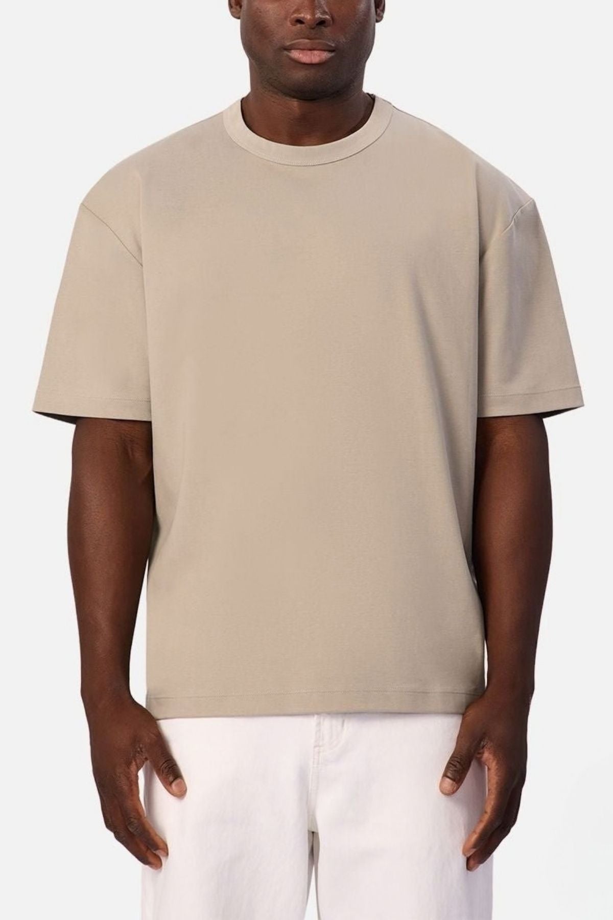 A person stands facing forward against a plain white background, wearing the Industrie Luxe Del Sur Tee in beige and white pants.