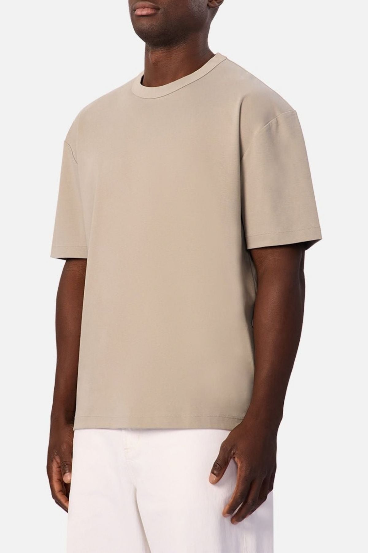 Wearing the Industrie Luxe Del Sur Tee—a loose-fitting beige t-shirt crafted from 100% cotton—paired with white pants, a person stands against a plain white background.