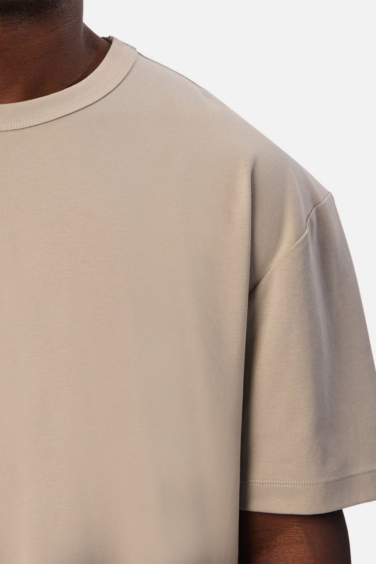 A close-up of a person wearing the Industrie Luxe Del Sur Tee in beige, crafted from 100% cotton, highlighting the upper chest, shoulder, and part of the arm against a simple light background.