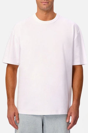 A man stands against a neutral background wearing the Industrie Luxe Del Sur Tee in plain white, crafted from 100% cotton, paired with light blue jeans.