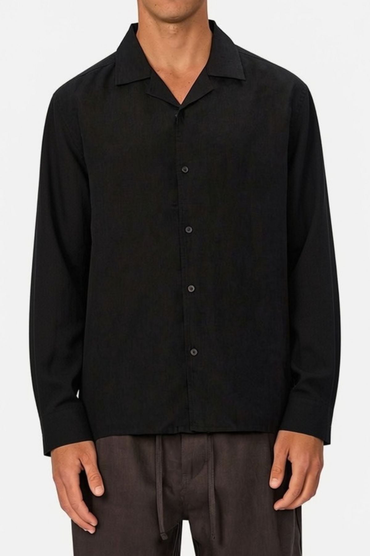 A man wearing the Industrie The St Martins Shirt, a regular fit, black, long-sleeved, button-up linen shirt with a collar, paired with dark drawstring pants, stands against a plain white background.