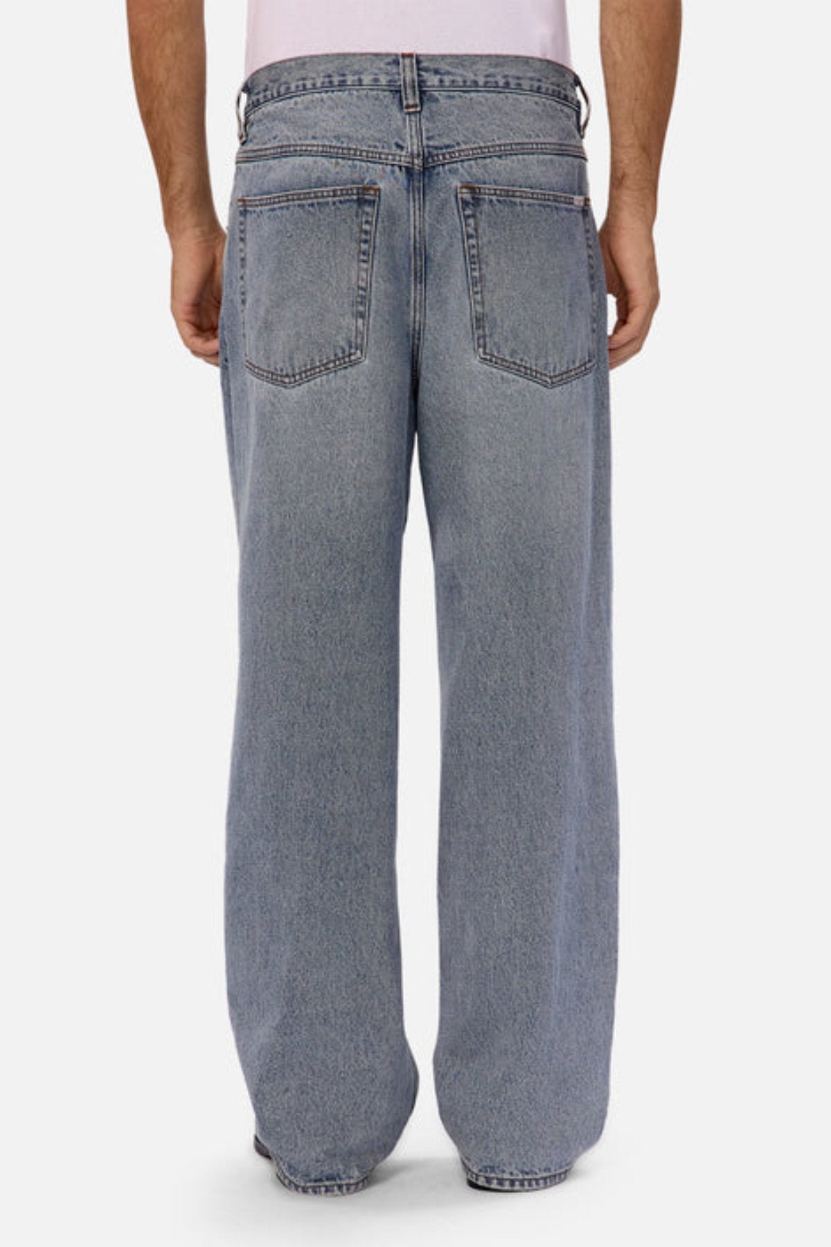 A person, shown from the waist down against a plain background, models Industrie The 80's Jean—vintage-inspired, light blue relaxed fit jeans with large back pockets—paired with a white shirt.