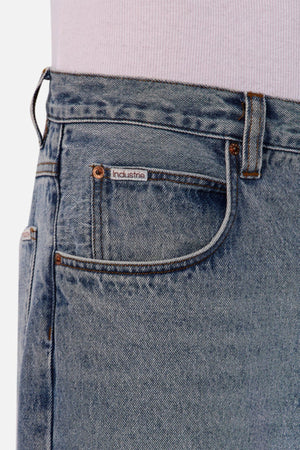Close-up of Industrie The 80's Jean in light blue vintage-inspired denim, featuring a front pocket with the "Industrie" label, visible stitching, a belt loop, and worn with a tucked-in light shirt.