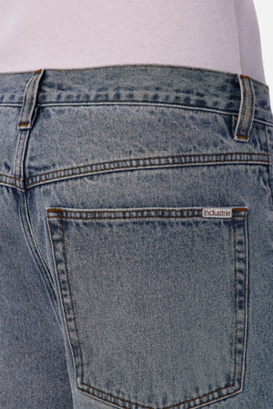 Close-up of the back pocket on Industrie The 80's Jean in light blue, vintage-inspired denim with a small "Industrie" label above the pocket. The durable waistband and lower part of a white shirt are also visible.