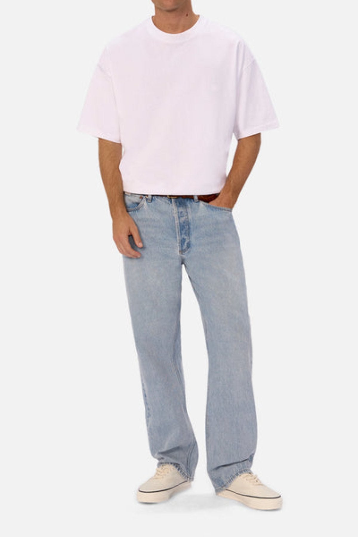 A person wears a loose white T-shirt, Industrie The 90's Jean—100% cotton vintage washed denim in a relaxed straight leg fit—and white sneakers, standing with one hand in their pocket against a plain light background.