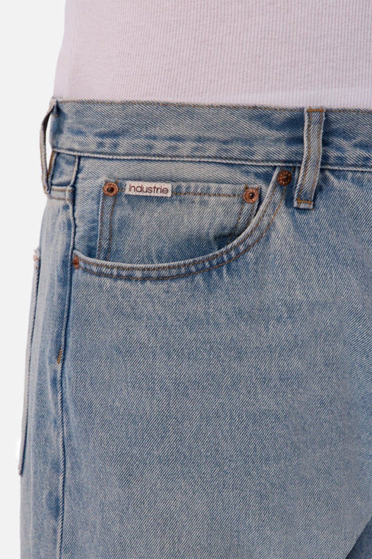 Close-up of a person wearing Industrie The 90's Jean, vintage washed with a relaxed straight leg fit and a small front pocket label, paired with a white ribbed shirt tucked in.