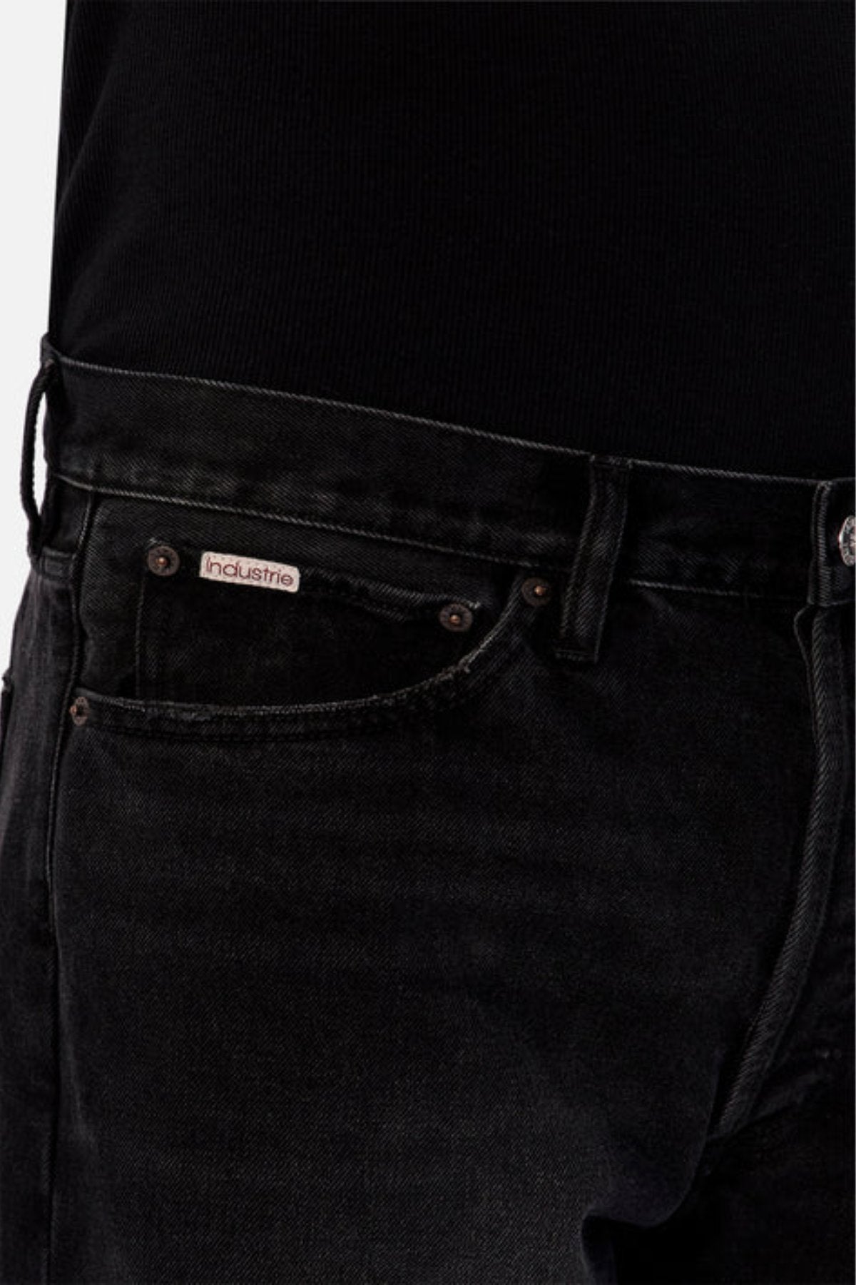 Close-up of a person wearing Industrie The 90's Jean in black vintage washed denim, featuring a relaxed straight leg fit and visible "Industrie" logo on the small pocket, paired with a black ribbed top. Only waist, pockets, and part of thigh are shown.