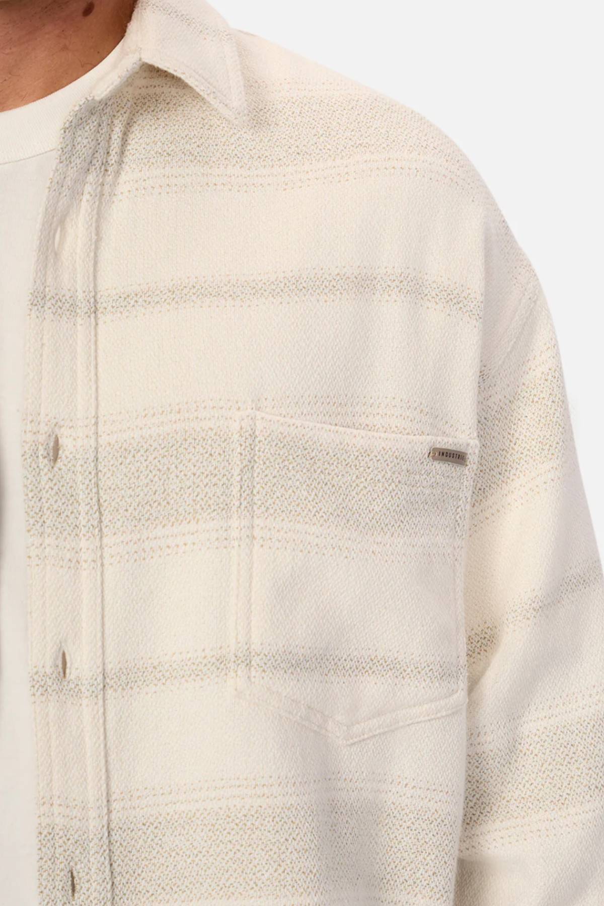 Close-up of a person wearing the Industrie The Arizona Long Sleeve Shirt in cream and light gray stripes over a white tee. This classic fit, 100% cotton shirt features a chest pocket with tag; only the lower face is visible.