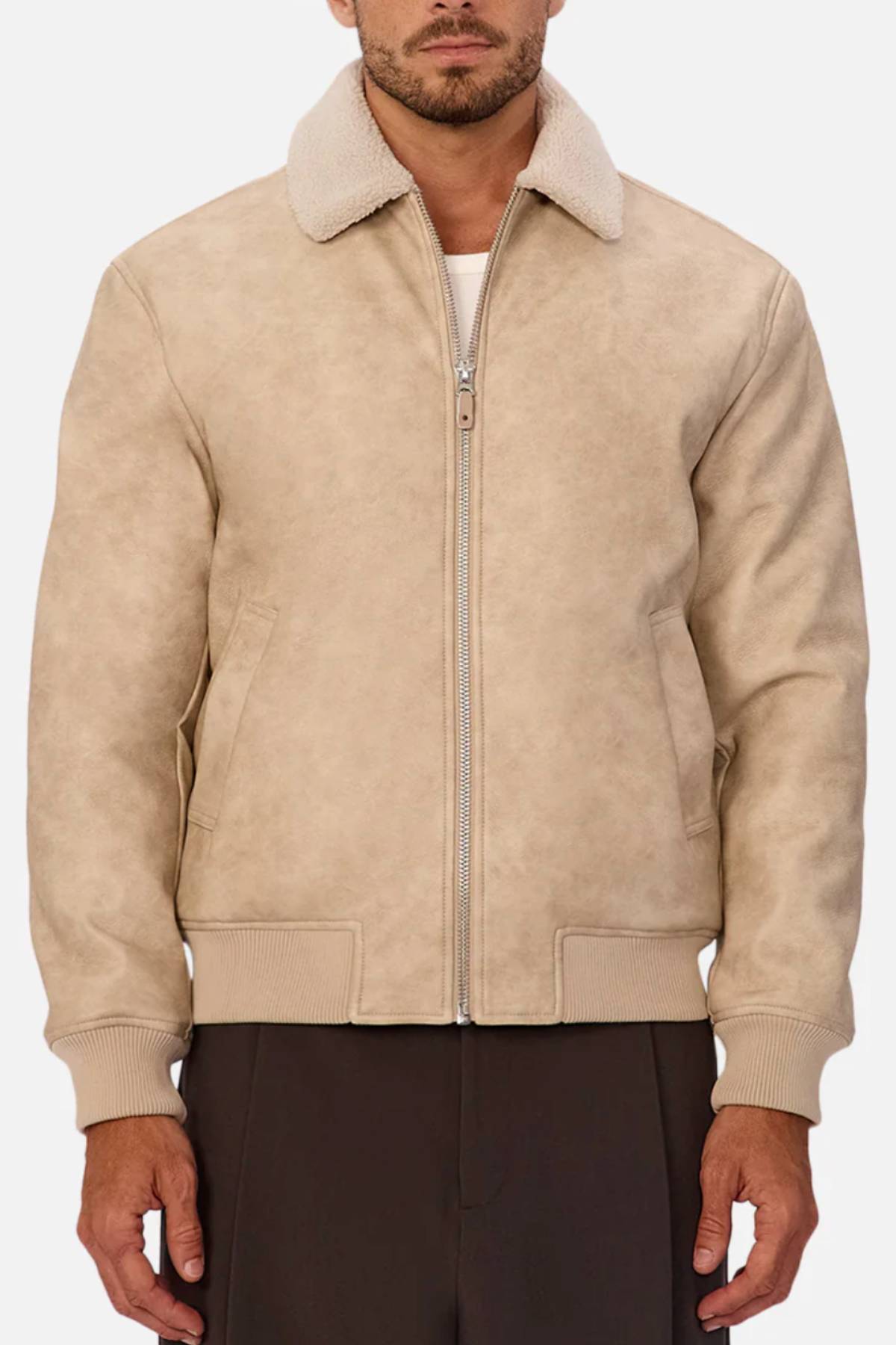 A man stands against a white background wearing the Industrie The Artem Flight Jacket, which features a beige PU leather body, Sherpa-look collar, front zipper, and ribbed cuffs and hem, styled over a white shirt and dark pants.