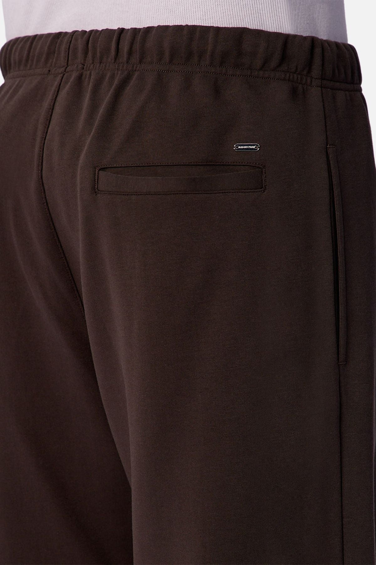 Close-up of the back of a person wearing Industrie The Astoria Lux Tech Trackpant in dark brown, featuring relaxed fit, elastic waistband, back pocket, and a small rectangular metal logo above the pocket for premium comfort.
