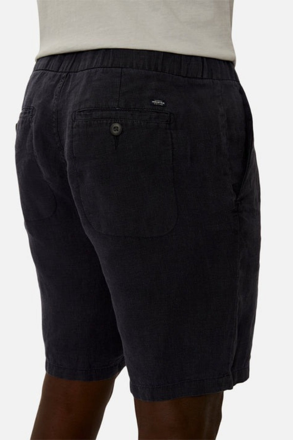 Back view of a person wearing the Industrie The Baller Linen Short, knee-length in dark gray with a buttoned back pocket. These linen shorts have a slightly textured appearance and are paired with a white top, enhancing their casual elegance.