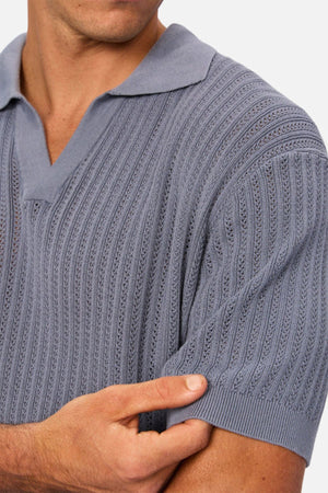 A man in the Industrie The Bellano Polo, a light blue short-sleeve 100% cotton knit shirt, holds his sleeve with one hand. His face is partially out of frame against a plain background.