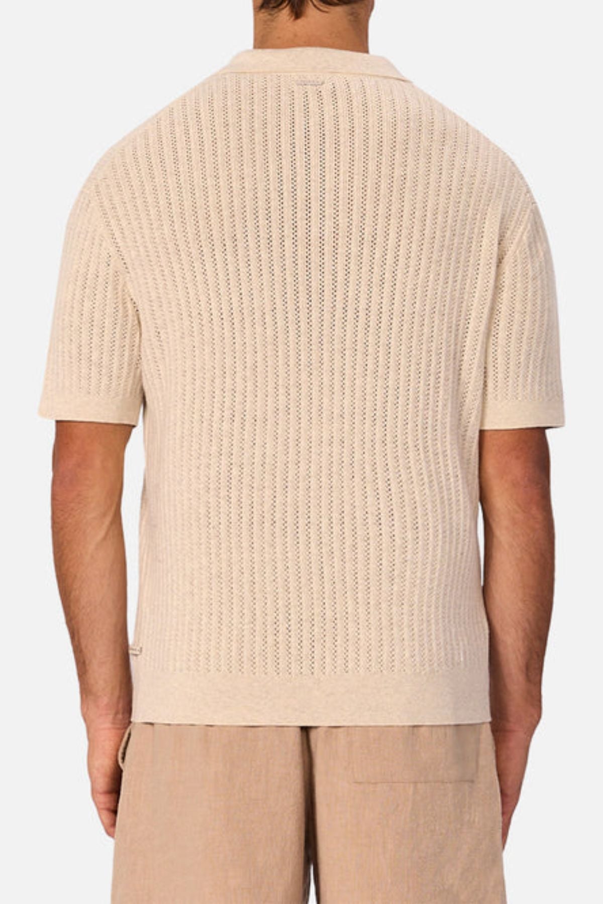 A man is shown from the back wearing a beige, short-sleeved Industrie The Bellano Polo— a breathable cotton men's knit with subtle vertical perforations—paired with light brown shorts.