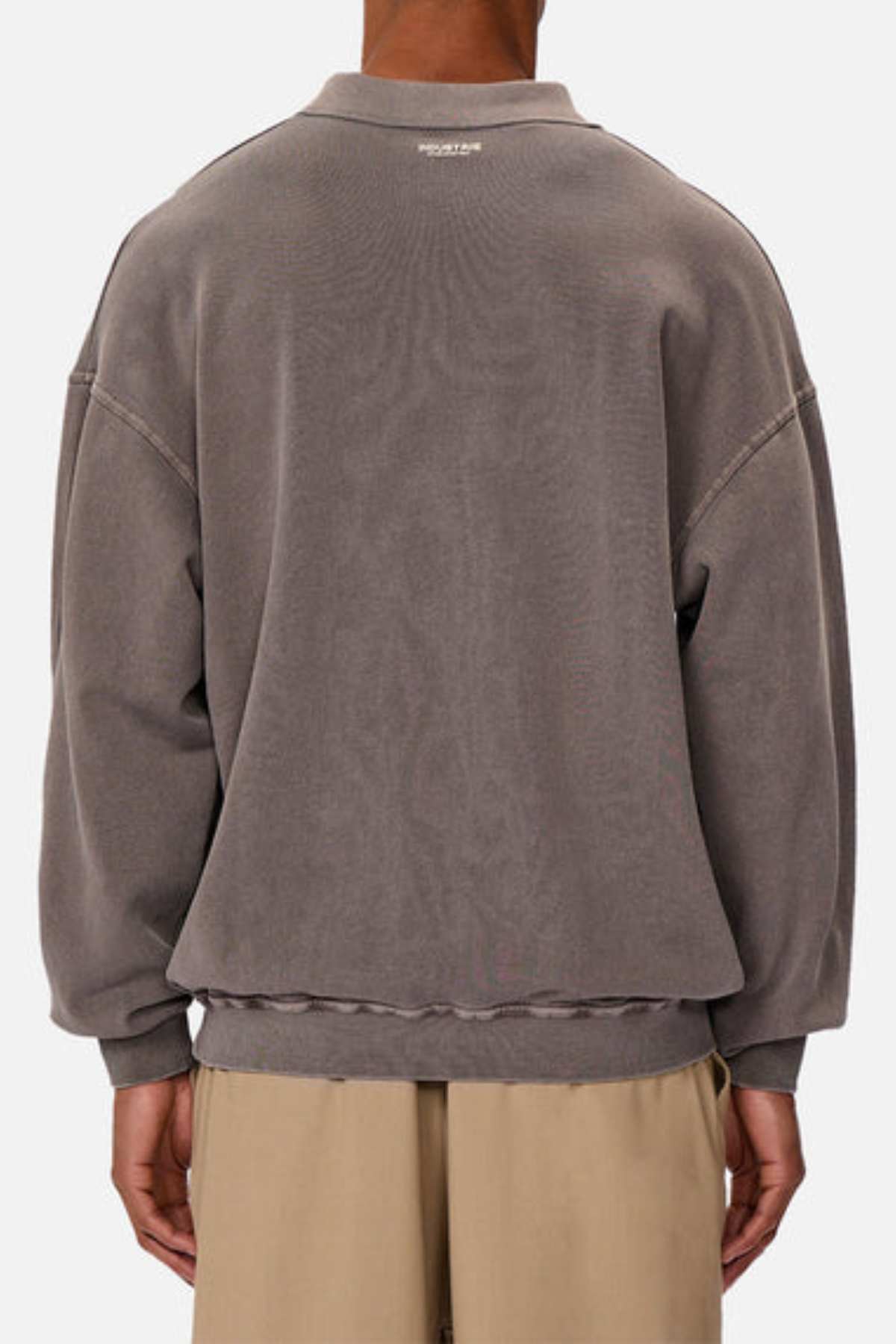 A person is seen from behind wearing the Industrie The Burbank Polo Track, a loose-fitting, faded gray premium sweatshirt with dropped shoulders, subtle neckline text, and beige pants set against a plain light background.