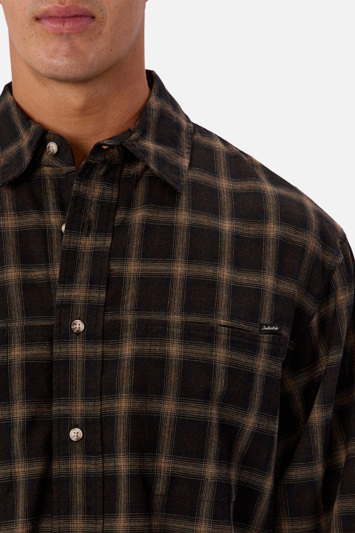 A person wears the Industrie The Carrington Shirt, a regular fit dark plaid checked shirt with beige and black stripes made from a premium wool blend, shown from shoulders to mid-chest against a plain light background with only the lower face visible.