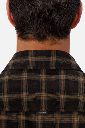 Close-up of the back of a person’s head, showing dark wavy hair and the collar of the Industrie The Carrington Shirt—a brown-and-black checked premium wool blend with "Indestructible" embroidered below the collar.