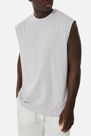 Someone wearing the Industrie The Del Sur Sleeveless Tee in light gray cotton paired with light-colored pants stands with one hand in their pocket against a plain background.