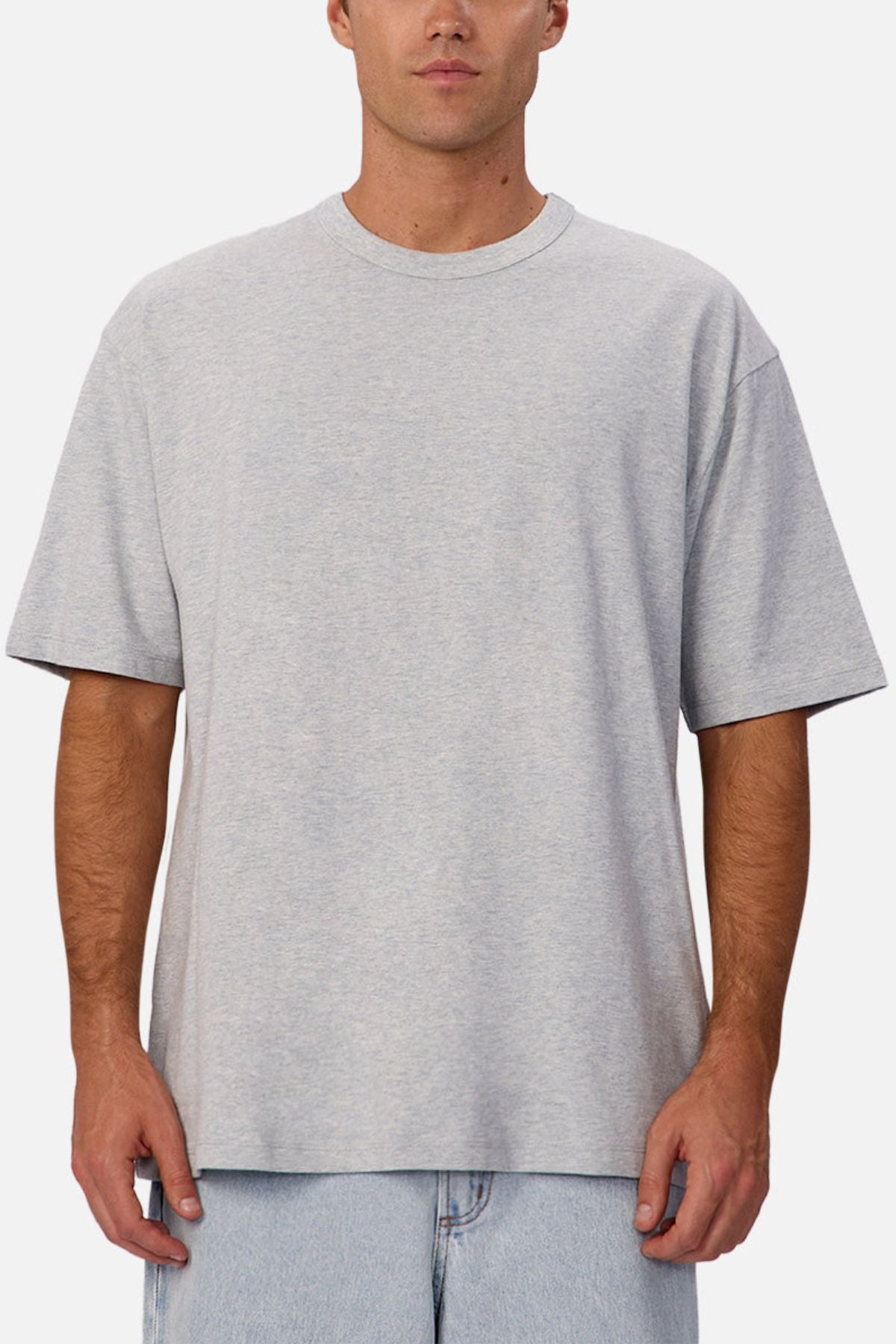 A man wearing an oversized light gray Industrie The Del Sur Tee made from heavyweight fabric and light blue jeans stands facing forward against a white background.
