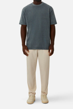 A person wearing an oversized fit faded blue Industrie The Del Sur Tee, light beige pants, and cream-colored sneakers stands facing forward against a plain white background.
