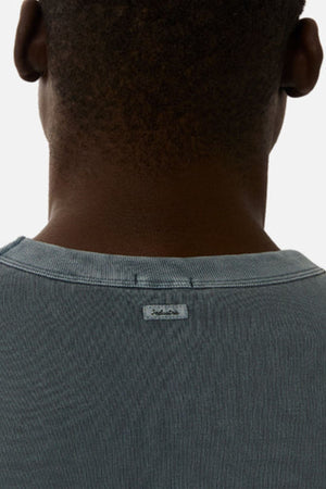 A close-up of the back neck and shoulders shows an oversized, light blue-gray Industrie The Del Sur Tee in heavyweight fabric, featuring a small fabric label sewn onto the neckline.