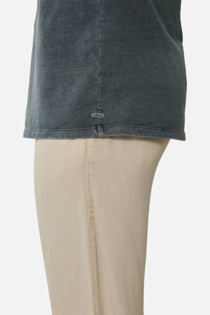 Side view of a person wearing an oversized, faded dark gray Industrie The Del Sur Tee and light beige pants, showing only the torso and upper legs against a plain white background.