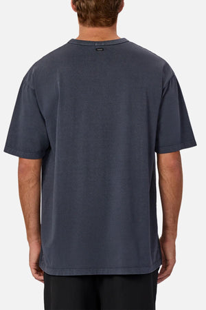 A person seen from behind wears an oversized, short-sleeve dark gray Industrie The Del Sur Tee and black shorts, standing against a plain light gray background.