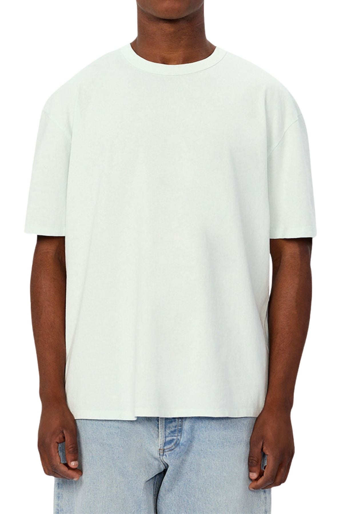 A person faces forward in an oversized Industrie The Del Sur Tee made from heavyweight fabric with a crew neckline and short sleeves, paired with light blue jeans. Their head is not visible, and the background is white.