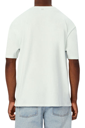A person is seen from the back wearing an Industrie The Del Sur Tee in plain light gray with short sleeves and a relaxed, oversized fit, paired with light blue jeans against a white background for a casual look.