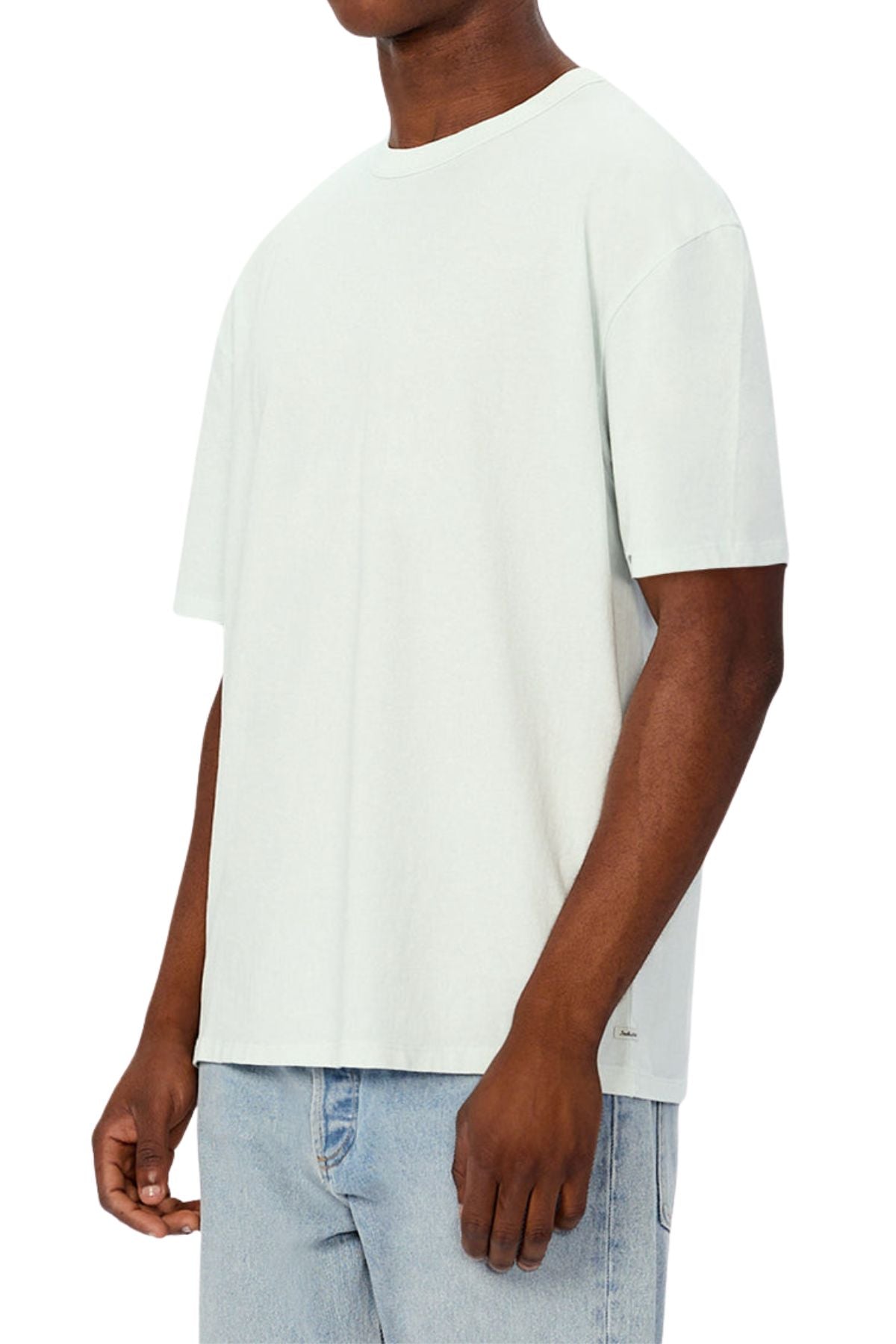 A person wears an oversized, light gray Industrie The Del Sur Tee made from heavyweight fabric with light blue jeans, standing against a plain white background, arms relaxed and head partially out of frame.