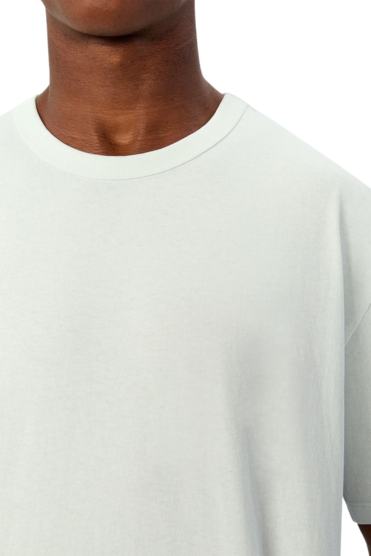A close-up of a person wearing the Industrie The Del Sur Tee in a light color with an oversized fit. Only the neck, shoulder, and upper chest are shown against a white background.
