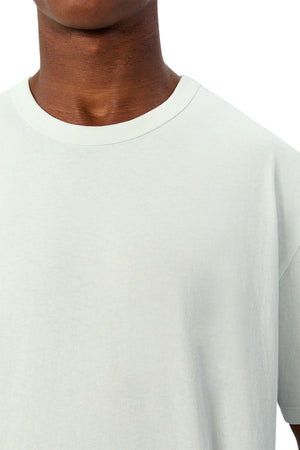 A close-up of a person wearing the Industrie The Del Sur Tee in a light color with an oversized fit. Only the neck, shoulder, and upper chest are shown against a white background.