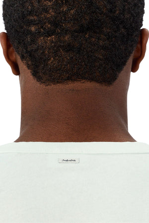 A close-up of the back of a person's head and neck reveals short, curly hair and the upper part of the light-colored Industrie The Del Sur Tee with a small "Industrie" label, showcasing its oversized fit.
