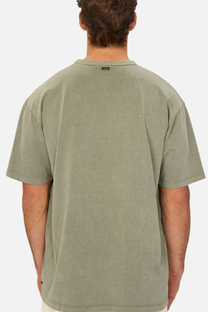A man with short brown hair is seen from behind wearing the Industrie The Del Sur Tee in heavyweight faded olive green and light shorts, set against a plain white background.