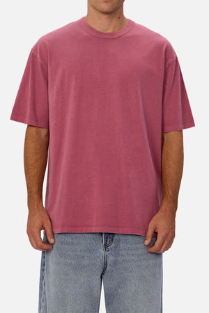 A person in an oversized, short-sleeve Industrie The Del Sur Tee in faded pink and light blue jeans stands against a plain white background. The tee’s heavyweight fabric gives it a relaxed look. Their head is not visible.