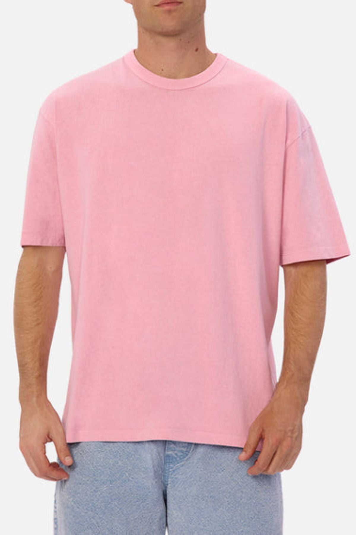 A person wearing the Industrie The Del Sur Tee, which has an oversized fit in pink, and light blue jeans stands against a plain white background.