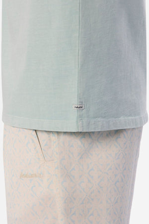 Zoomed-in view of an Industrie The Del Sur Tee in light blue, slightly tucked into cream shorts with a delicate geometric design. This oversized tee showcases a small tag near the hem, and the shorts have a discreet logo above the pocket, capturing a casual and minimalist aesthetic.