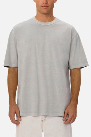 A man wearing an oversized Industrie The Del Sur Tee in light gray and off-white pants stands facing forward against a plain white background.