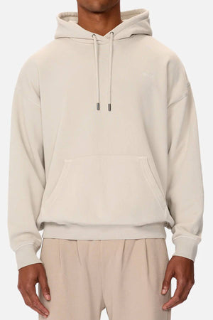 A person wearing the Industrie The Del Sur Washed Hoodie in an oversized beige fit with a front pocket and drawstrings, paired with matching light beige pants, stands against a plain white background.