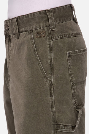 Close-up of a person wearing Industrie The Detroit Carpenter Pant in olive green 100% cotton canvas, with visible stitching, belt loops, button closure, and multiple pockets. Paired with a tucked-in white shirt for a sharp street style look.