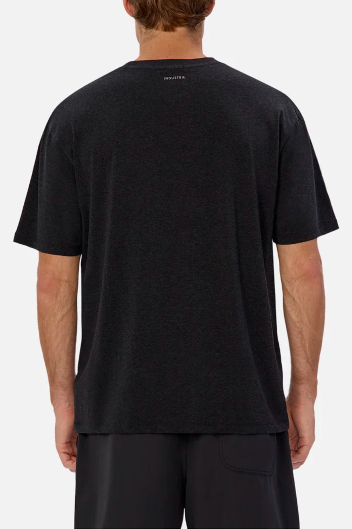 A man is shown from the back wearing the Industrie The Freeman Athletic Tee, a relaxed fit, short-sleeved black T-shirt with a lightweight feel and a small white logo near the neckline, paired with black shorts.
