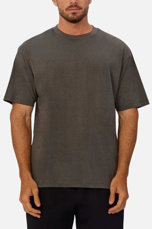 A man faces forward in the Industrie The Freeman Athletic Tee, a relaxed fit, short-sleeve athletic top in charcoal grey, paired with black pants against a plain light background.