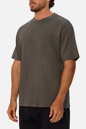 A man wears the Industrie The Freeman Athletic Tee in dark gray with black pants, standing against a plain light background. His face is partially visible, and his hands rest relaxed at his sides.
