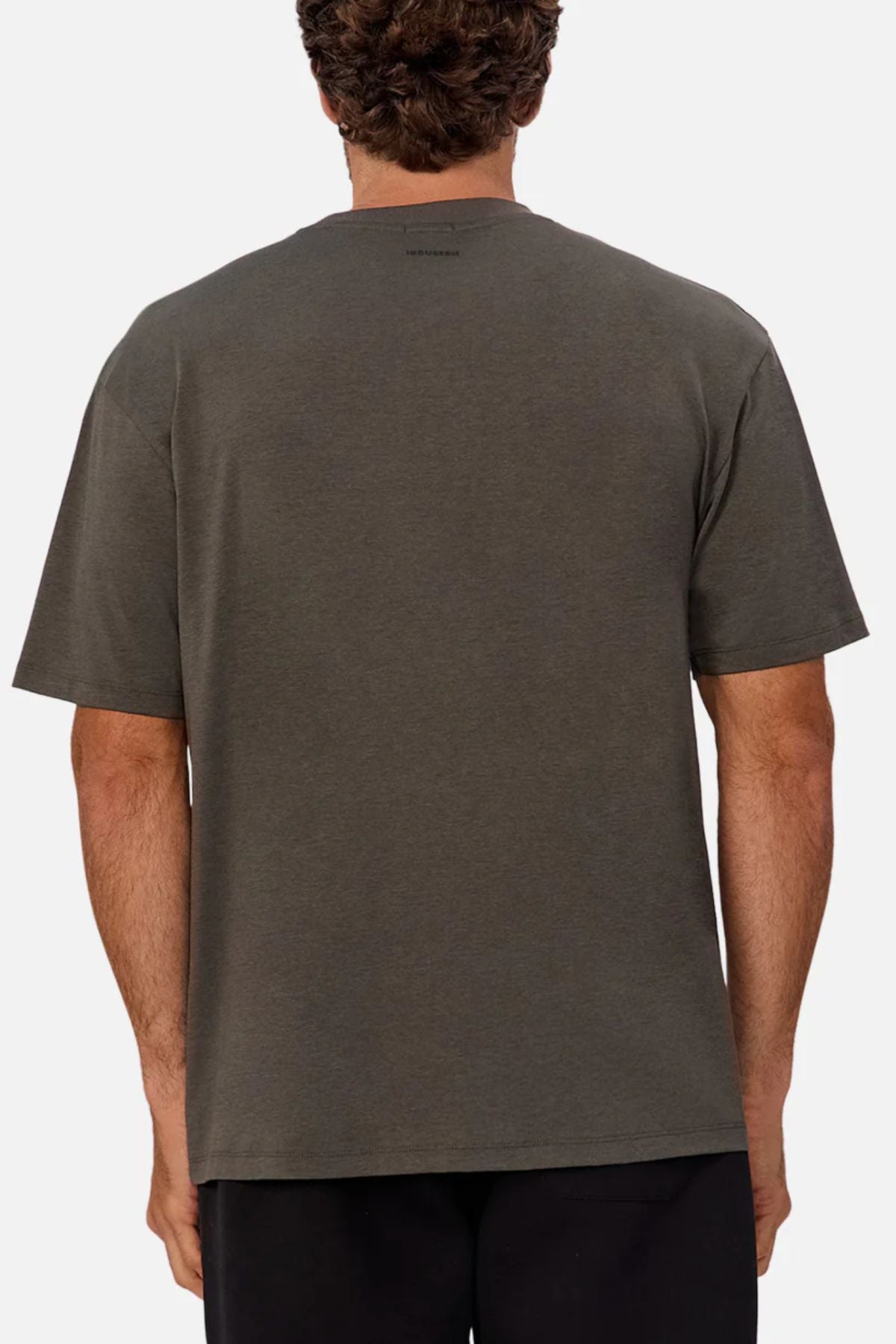 A person with short curly hair is seen from the back, wearing the Industrie The Freeman Athletic Tee in dark gray and black pants against a plain light background.