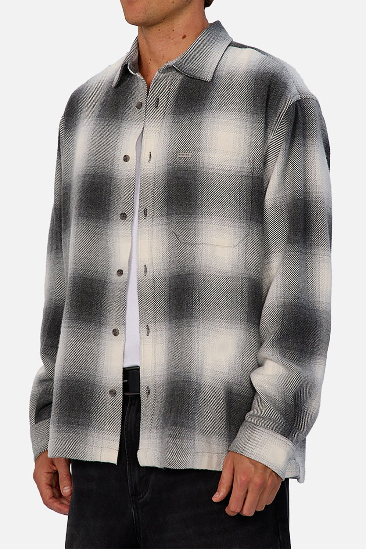 A person wears the Industrie The Highland Shirt in a black, gray, and white shadow check pattern over a white T-shirt with dark pants. The collared, long-sleeve shirt has a tailored fit and is shown from shoulders to mid-thigh.