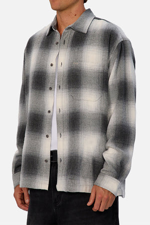 A person wears the Industrie The Highland Shirt in a black, gray, and white shadow check pattern over a white T-shirt with dark pants. The collared, long-sleeve shirt has a tailored fit and is shown from shoulders to mid-thigh.