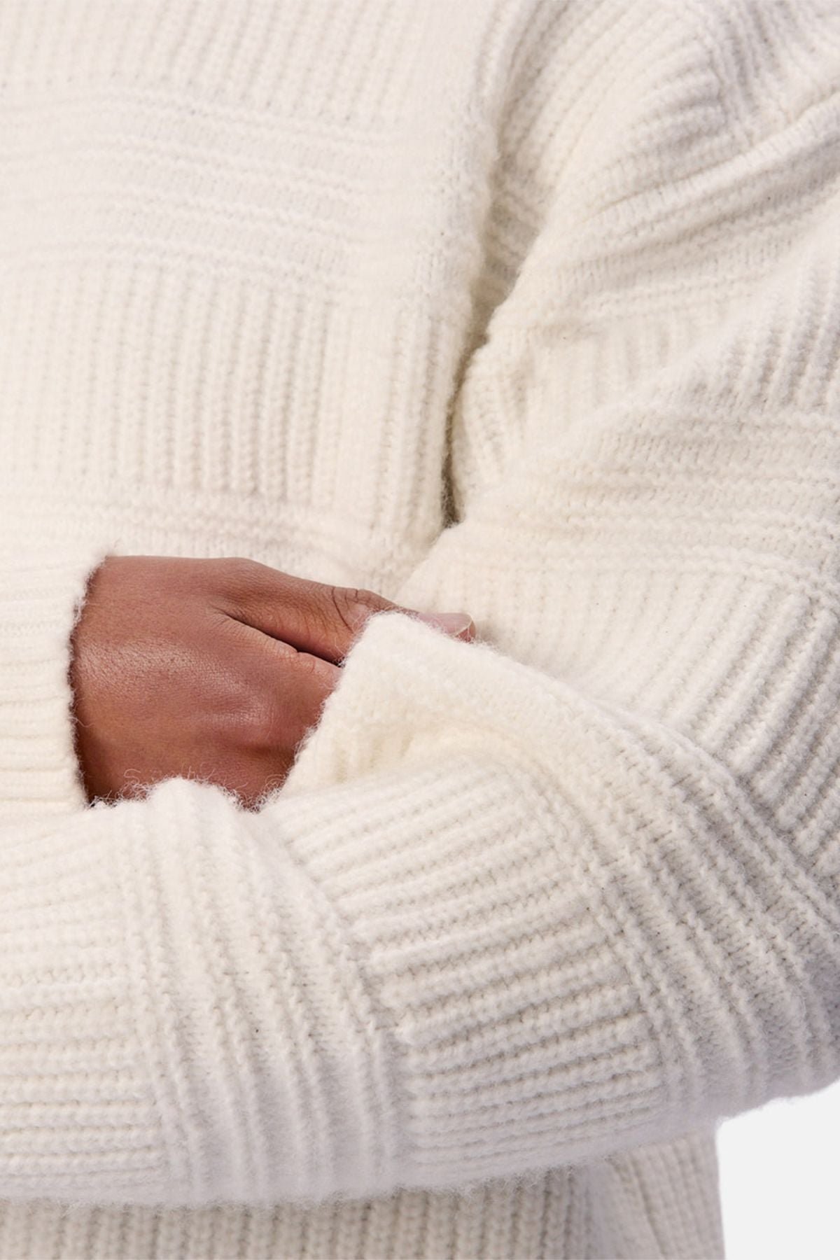 Someone wearing the Industrie The Huntington Knit, a chunky white crew neck sweater, crosses one arm over their body with their hand tucked into the opposite sleeve.